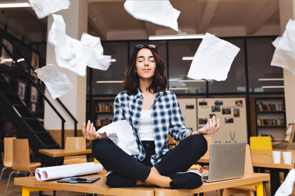 Woman meditating on her desk in the middle of the office