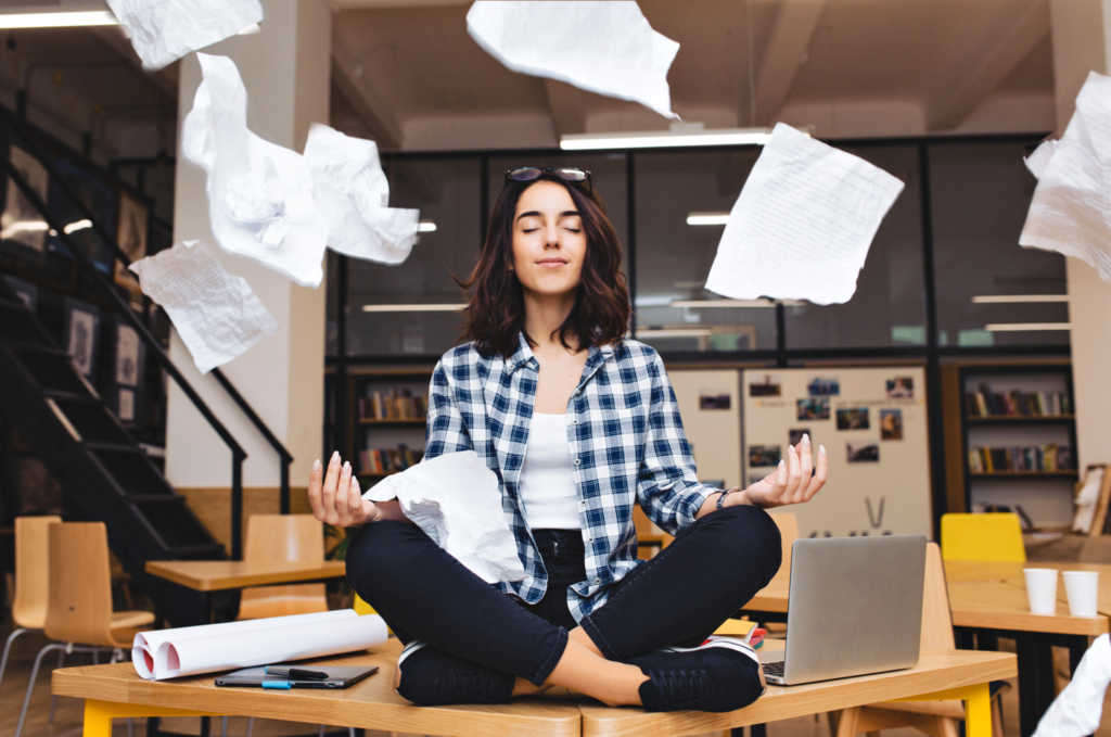 Woman meditating on her desk in the middle of the office at work